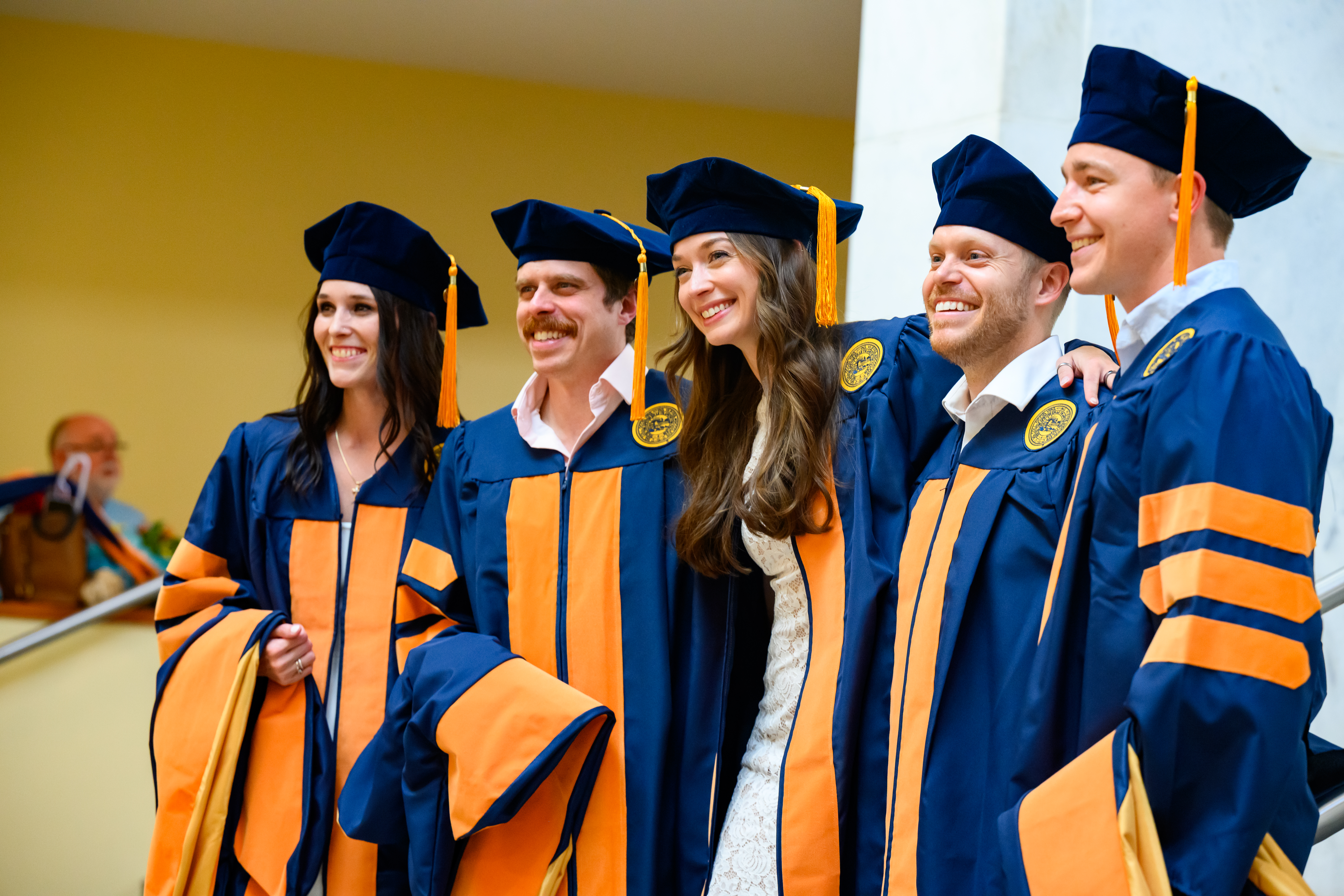 Nursing students in graduation regalia smile and pose for a photo with their arms around each other.