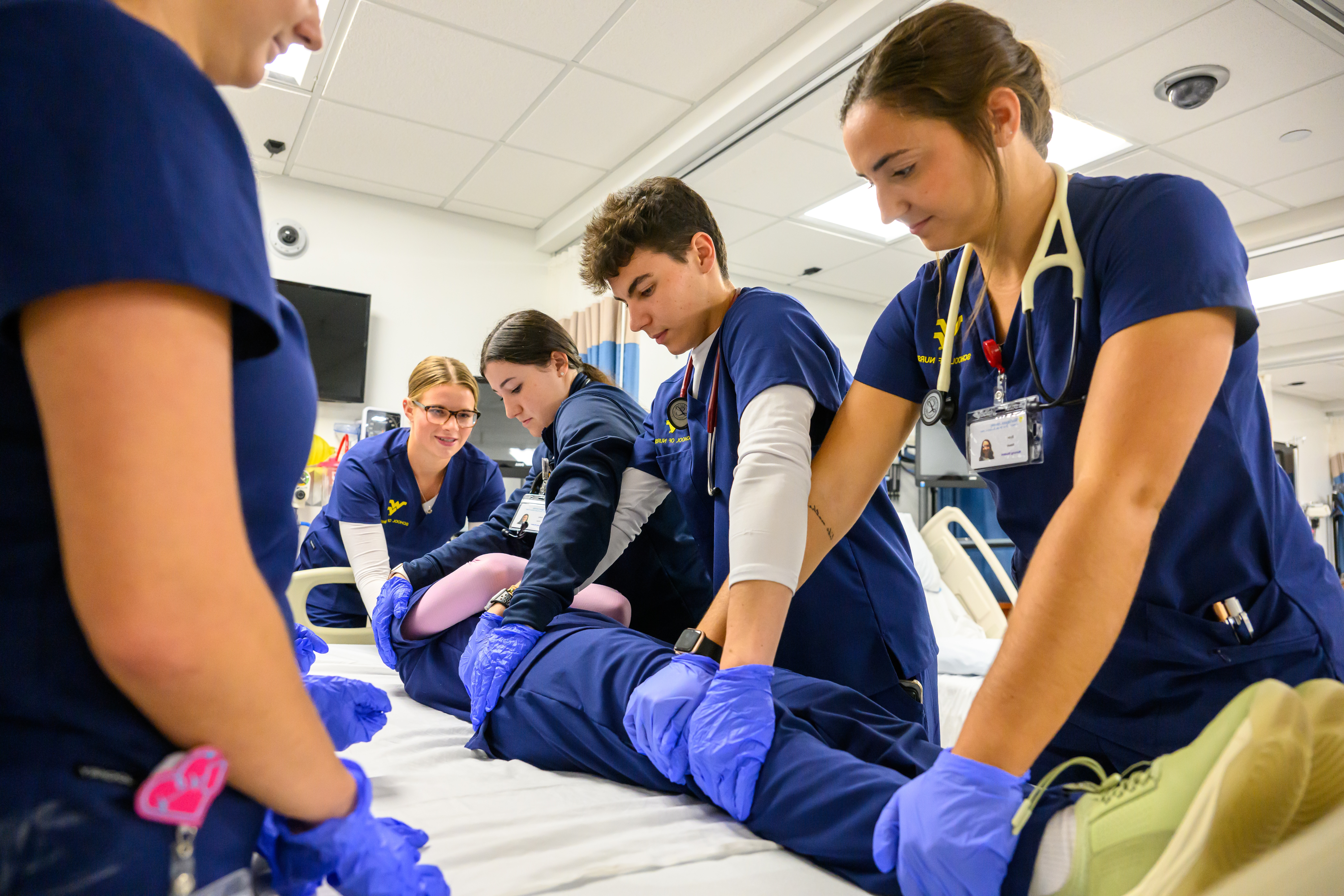 Four nursing students practice rotating a manikin in the hospital bed. 